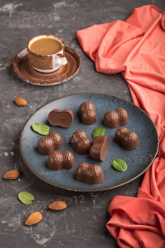 Chocolate candies with almonds and a cup of coffee on a black concrete background and red textile. Side view, close up
