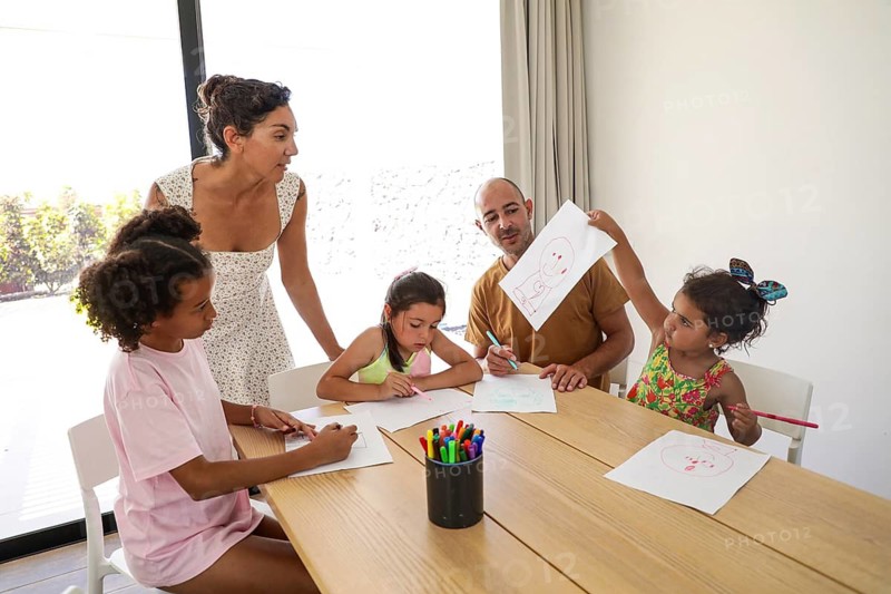 A joyful family gathers around a table to enjoy drawing and creativity at home. Parents and children engage in art, sharing laughter and bonding moments in a cozy room