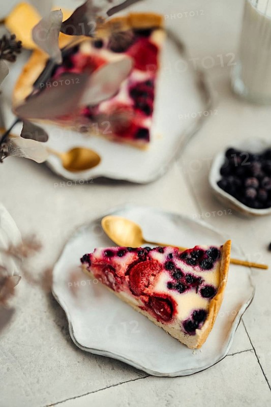 Top view of a berry clafoutis pie slice, richly topped with blackcurrants and strawberries, elegantly presented on a ceramic plate