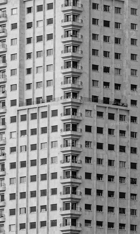 Black and white close-up of a modern high-rise residential building with multiple balconies in Madrid, capturing the urban architecture and dense living spaces