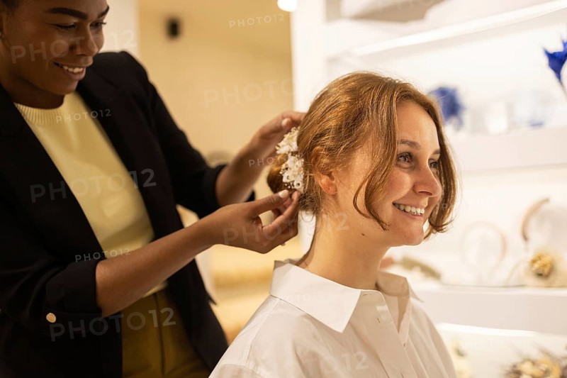 A joyful woman receives the final touches on her hair with a delicate floral accessory. Captured in a bright, elegant setting, this image exudes care and preparation