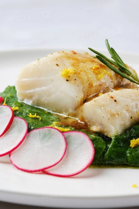 A tender white fish fillet is elegantly placed atop vibrant wilted greens. Fresh radish slices and citrus zest add a burst of color and flavor, creating a refined culinary presentation