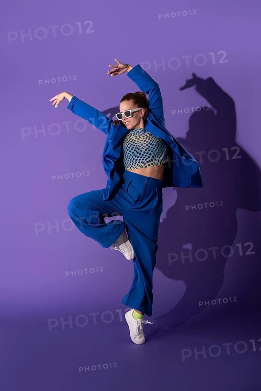 A dynamic young woman dancer elegantly poses against a vivid purple background, clad in a stylish blue outfit, capturing the grace and energy of modern dance