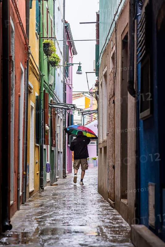 City view of Burano with colourfully painted houses and canals. Rainy weather, people are carrying umbrellas. Burano, Venice, Venezia, Italy