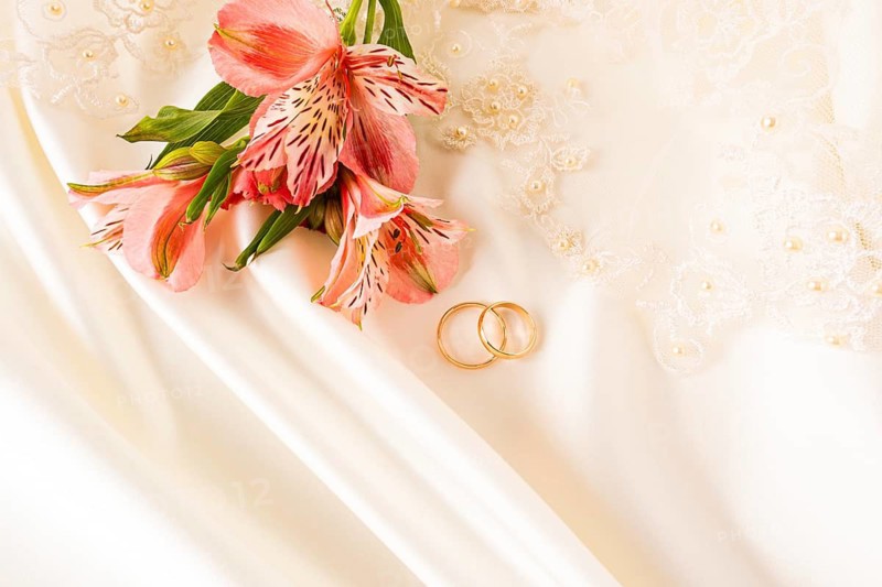 Elegant wedding rings are beautifully displayed with vibrant pink flowers atop a delicate lace fabric, creating a romantic and sophisticated wedding theme scene