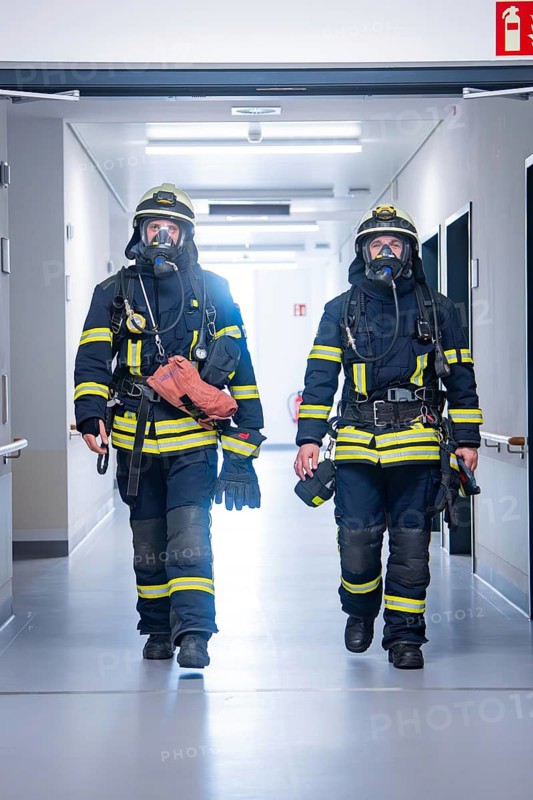 Two firemen in full gear walk down a corridor, fire brigade exercise on blue light day in the new Calw hospital, Germany