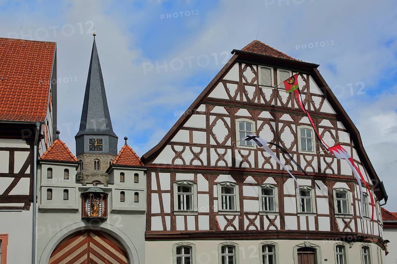 Heimatspielhaus with coat of arms and spire of St. Maria Magdalena, half-timbered house with flags, Münnerstadt, Rhön, Lower Franconia, Bavaria, Germany