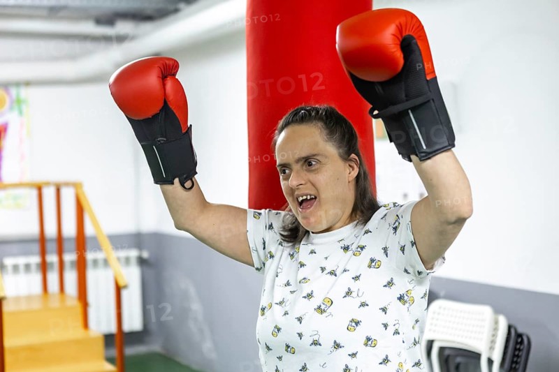 A woman wearing boxing gloves raises their arms triumphantly in a mental health residence, symbolizing empowerment and resilience through physical activity