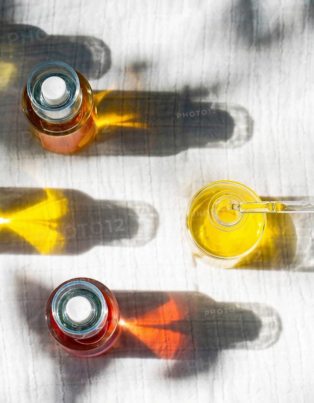 Overhead view of natural body oils infused with plants like calendula and rose. The image captures the vibrant colors of oils in glass bottles casting shadows