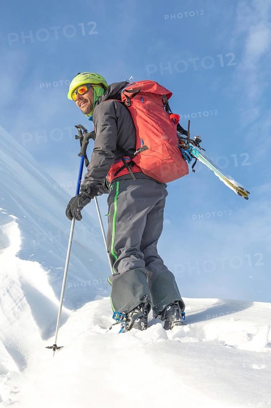 A skier, equipped with a backpack and ski poles, enjoys a sunny day on a snow-covered mountain slope, perfect for ski touring and exploring the winter landscape