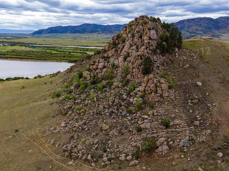 Rocky outcrops rise above the lush greenery near Vladivostok, Russia. The scene captures a mix of stones and trees beside a winding river under a cloudy sky. Nature's beauty invites exploration and appreciation of the outdoors