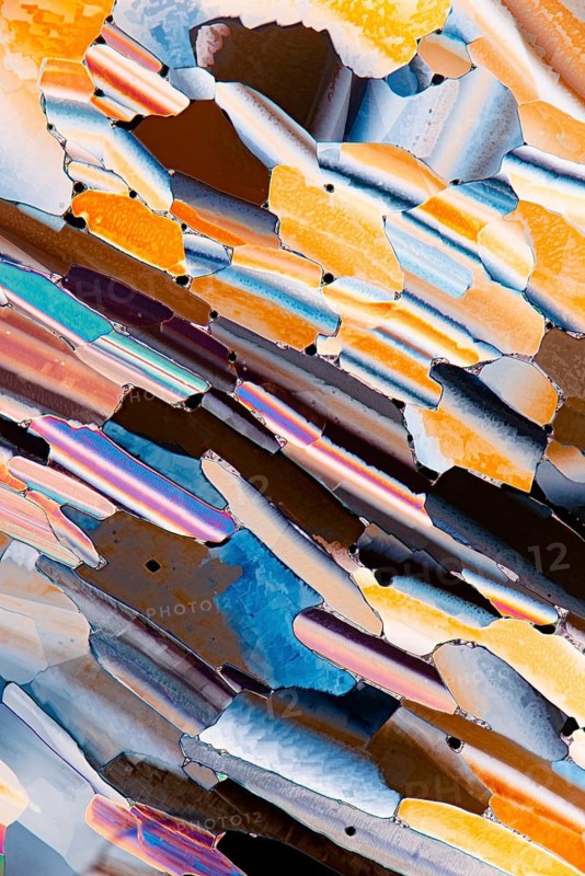 A colorful microscopic view of liquid crystals featuring an array of vivid oranges, blues, and reflective hues