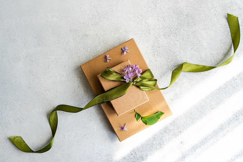 Two brown gift boxes adorned with a green ribbon and purple flowers are elegantly displayed on a light background, evoking a sense of celebration and elegance