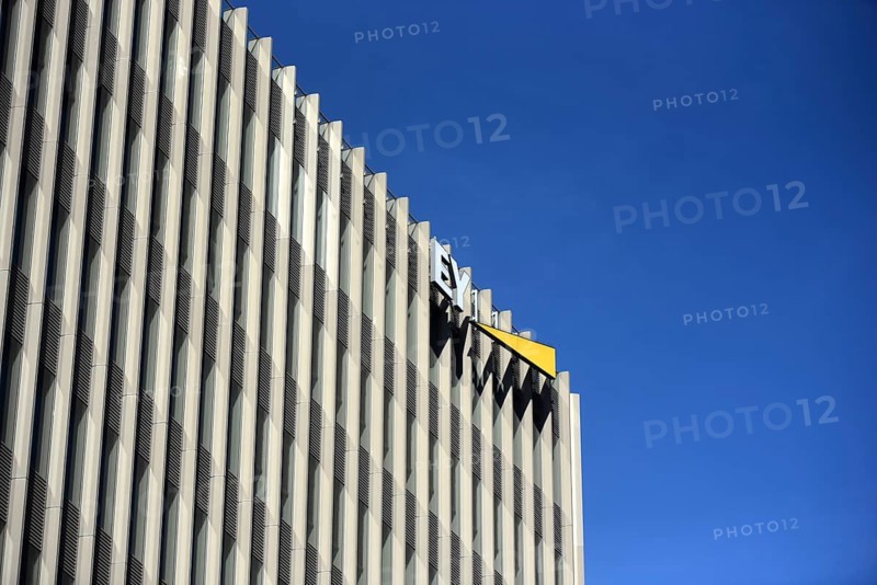 The façade of a modern EY office building with repetitive vertical slats, clear lines and a company sign, against the contrast of a bright blue sky, a minimalist architectural detail that highlights geometry and light. EY logo below the roof