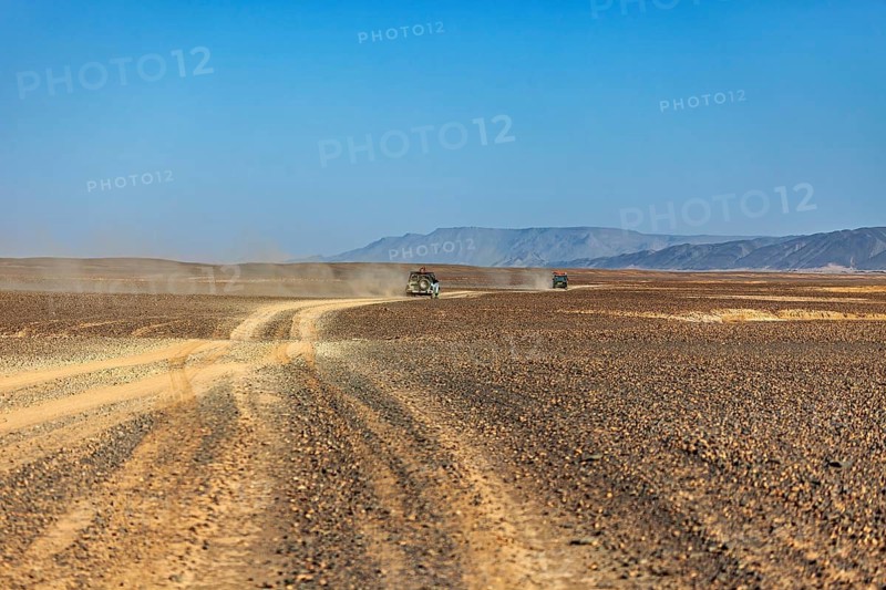 Car travelling on a dusty road through a vast landscape, mountains in the distance, Off-road vehicle through the endless landscape of the Sahara desert in Algeria