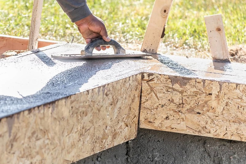 Construction Worker Using Wood Trowel On Wet Cement Forming Coping Around New Pool