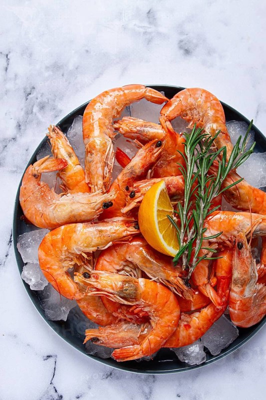 Freshly frozen shrimp on ice, with lemon and rosemary, on the marble table, top view, no people