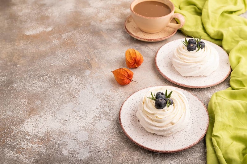 Pavlova Meringue dessert with crisp meringue and blueberry, cup of coffee, on brown concrete background with green linen textile, copy space, side view