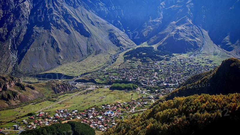 City nestled in a valley with surrounding mountains, clear view, Stepantsminda, Caucasus, Georgia