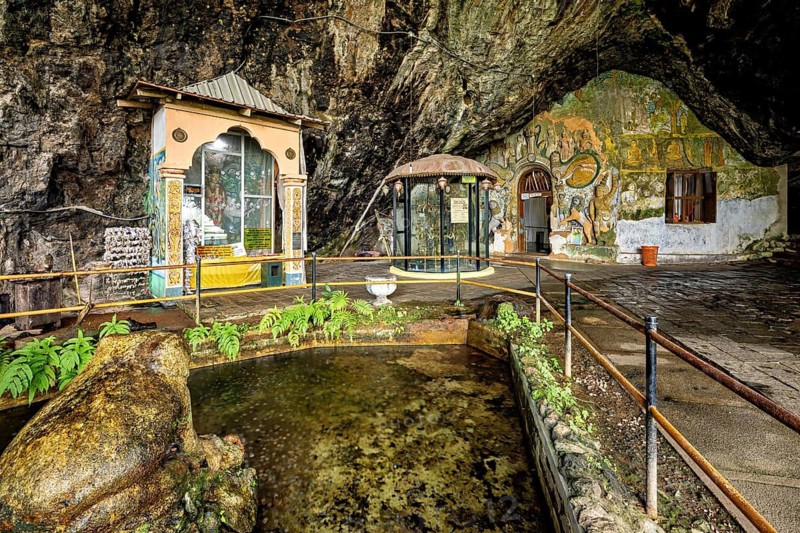 Interior of a cave with a small pond, sculptures and painted walls surrounded by vegetation, The Diva Guhawa cave temple near Ratnapura in Sri Lanka
