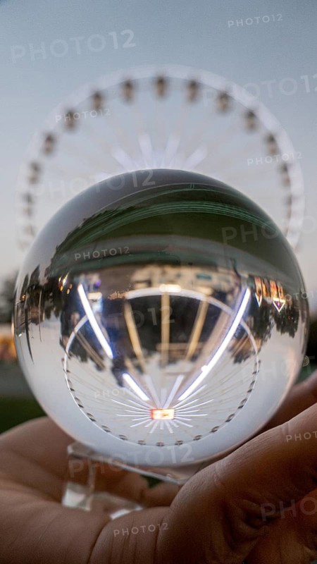 Cropped unrecognizable person's hand holding a crystal sphere looking through the Chicago Ferris wheel ingeniously reflected on crystal, with a blurred background in Geneva, Switzerland