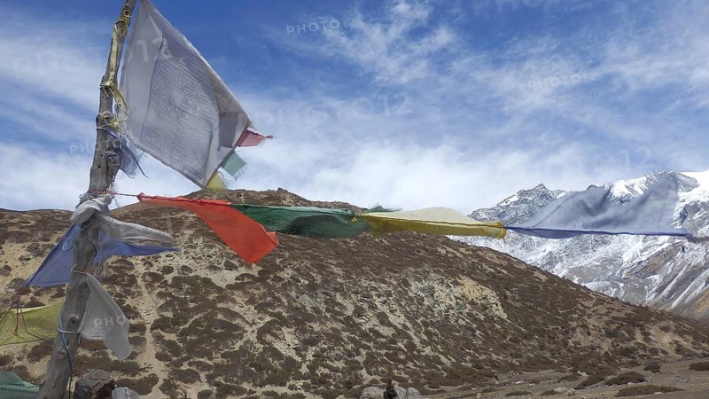 Fanned prayer flags fly against a cloudy sky over a mountainous landscape, trekking at Annapurna Circuit, Manang, Nepal
