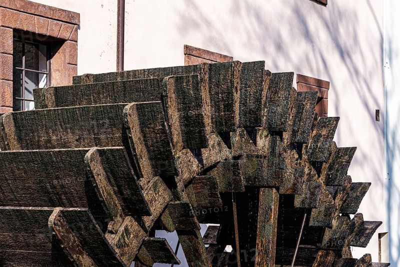 A close-up of a traditional wooden waterwheel against a historic Prague building, showcasing rich textures and architectural elements characteristic of old Prague