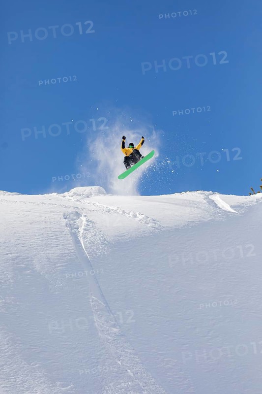 A snowboarder performs an aerial stunt on a snowy slope, set against a vibrant blue sky. The image captures the thrill and freedom of snowboarding in winter scenery