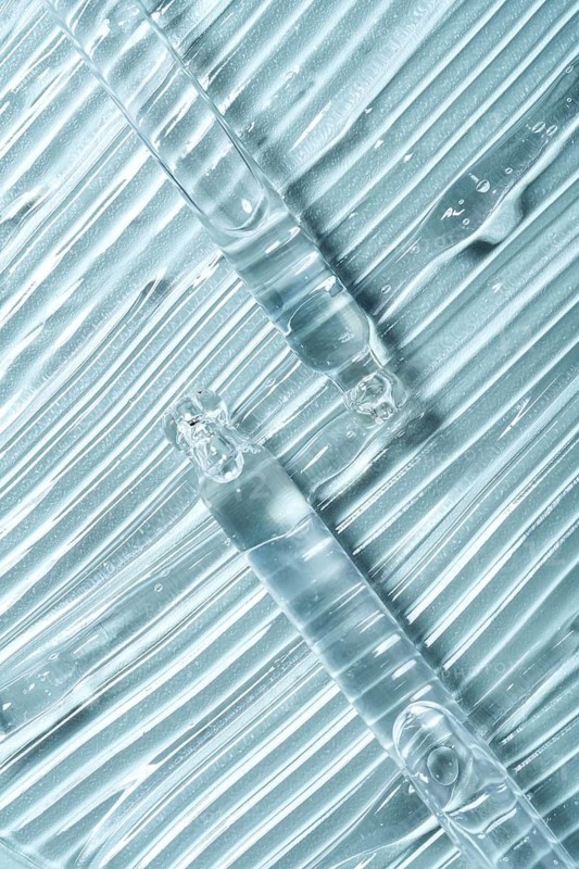 Top view of transparent gel smears with pipettes on clear glass. The texture and shine illustrate a laboratory setting, evoking themes of scientific and cosmetic innovation