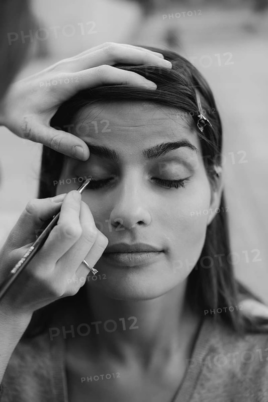 A makeup artist carefully applies eyeliner to a client's eyelid in a close-up black and white shot, showcasing precision and artistry in makeup application
