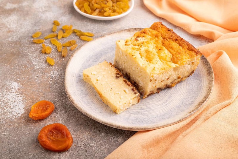 ?ottage cheese ?asserole, Curd cake, with dried apricots and raisins on brown concrete background and orange textile, side view, close up, minimalism
