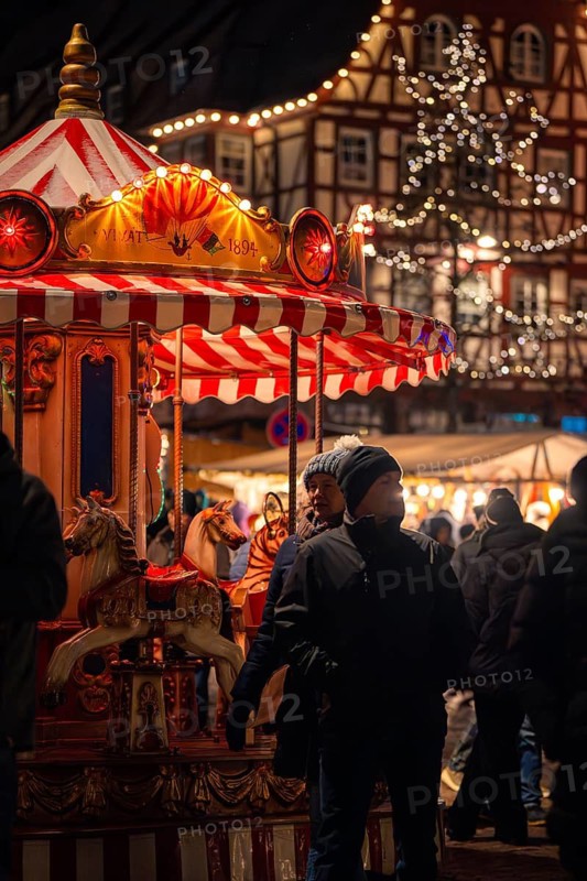 Illuminated carousel at a Christmas market, surrounded by people and traditional buildings, Christmas market Calw, Black Forest, Germany