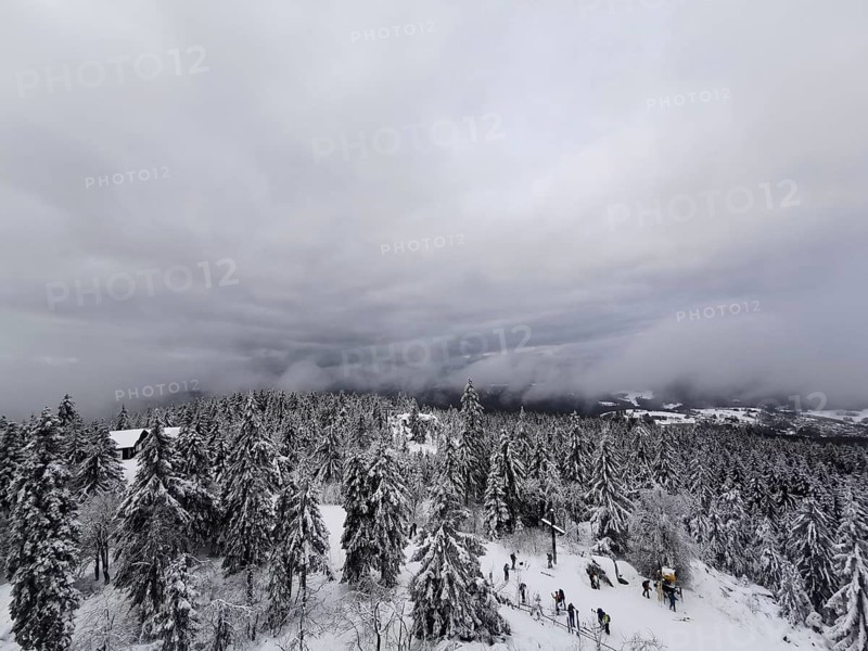 View from the Asenturm on Ochsenkopf, people hiking through a snow-covered forest under a foggy sky, hiking in the Fichtelgebirge nature park Park