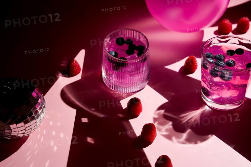 A vibrant scene with refreshing pink drinks in glasses with blueberries and raspberries. The pink background and disco ball create a festive and fun atmosphere