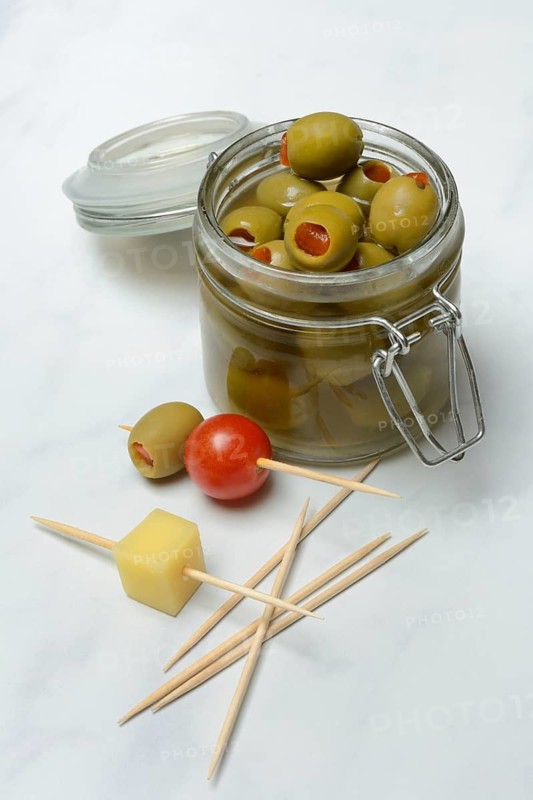 Green olives in glass and on toothpicks with tomato and cheese cubes