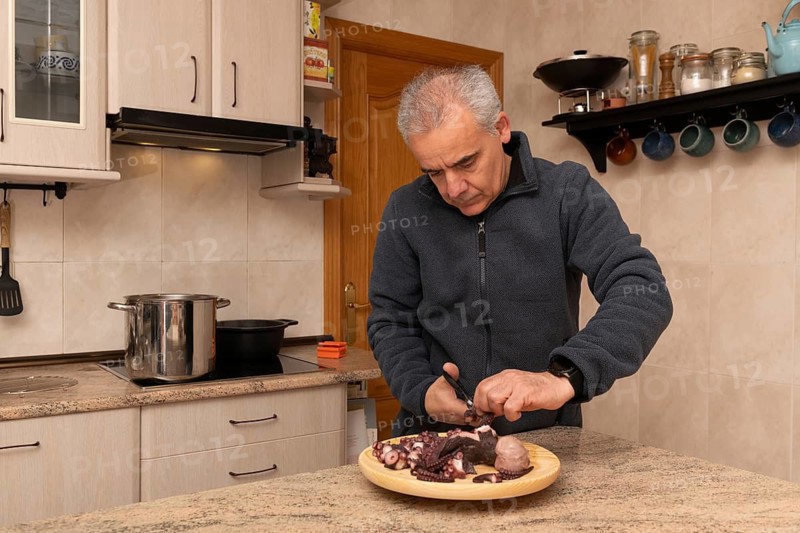 A man skillfully preparing octopus in a contemporary kitchen with various utensils and ingredients around. The image captures a moment of culinary focus and precision