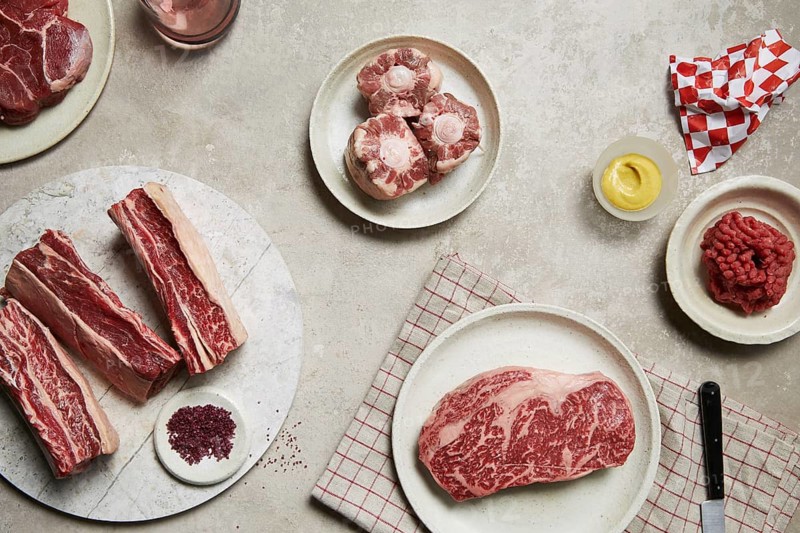 An assortment of fresh meats arranged on plates, showcasing different cuts like steak, oxtail, and minced beef. Perfect for illustrating a butcher's quality offerings
