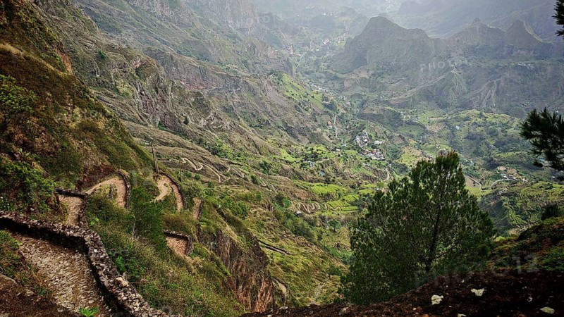 Panoramic, panoramic view of a winding path, hiking trail along a mountain range with green slopes and a foggy valley, hiking from Cova Crater through Paul Valley, Ribeira do Paul to Vila das Pombas, Cova nature park Park, Santo Antao, Cabo Verde, Cape Verde, Cape Verde