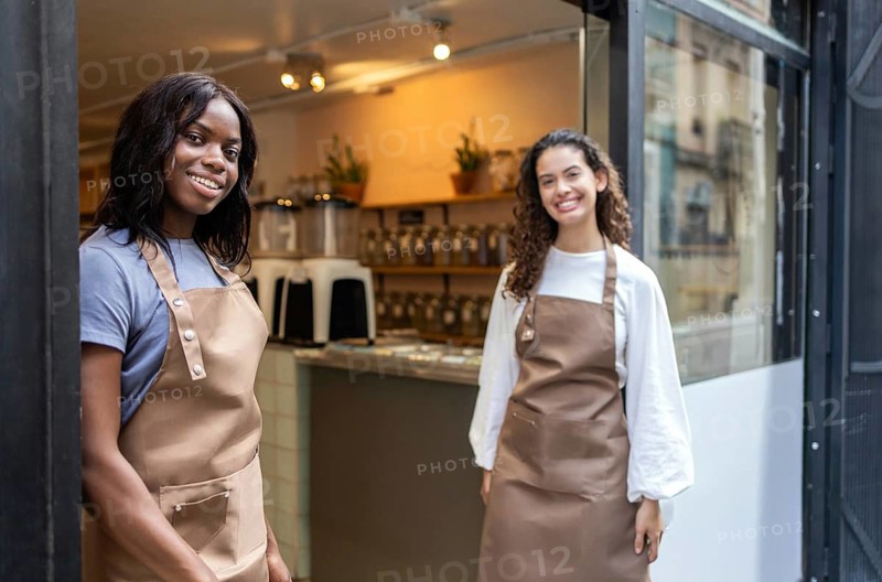 Two clerks warmly welcome customers at an organic bulk store. The cozy atmosphere is enhanced by natural lighting, fresh products, and a focus on sustainability and community