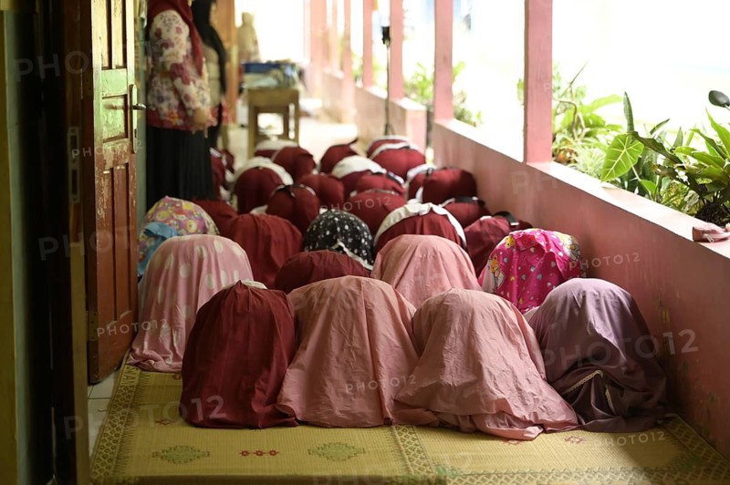Back view of unrecognizable women dressed in traditional burqa and hijab kneeling in prayer, on a mat-covered floor. Engaging in a spiritual or religious activity in a peaceful, indoor setting, demonstrating cultural or religious practices
