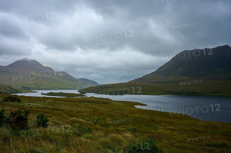 Grassy hills with a lake under a thick, cloudy sky, Loch Bad a Ghaill, Badnagyle, Ullapool, Scotland, United Kingdom, Great Britain