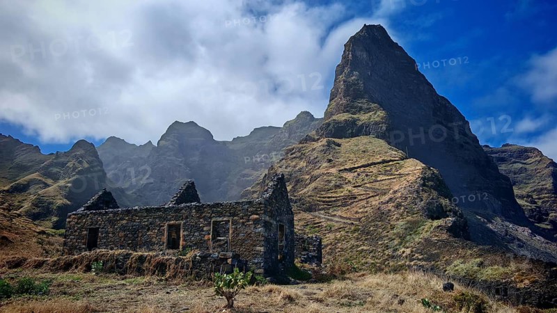 Ruin in front of a majestic mountain peak with clouds and clear sky, hiking, lost place, abandoned village of Formiguinhas, Marinha da Cruzinha natural park, Santo Antao, Cabo Verde, Cape Verde, Cape Verde