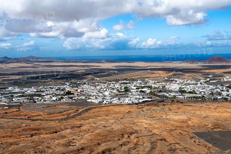 View of town, white houses of Teguise with church tower in dry volcanic landscape, view from Guanapay volcanic crater, Lanzarote, Canary Islands, Spain