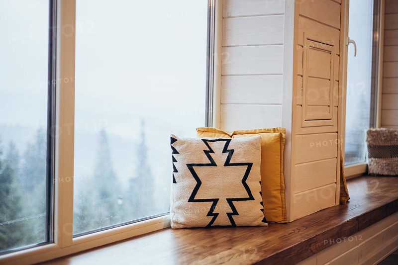 A snowy landscape is visible through a large window, enhanced by a comfortable window seat adorned with stylish yellow and patterned pillows, creating a serene and inviting indoor scene