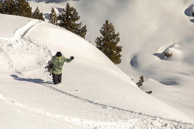 A snowboarder hikes up a snowy mountain in search of an exhilarating freeride adventure in untouched backcountry powder, embracing the thrill of winter sports