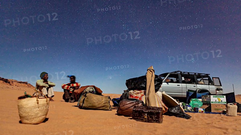 Night in the desert with two people next to a car full of luggage under a clear starry sky, Tuareg sitting at night in the dunes of the Sahara in Algeria