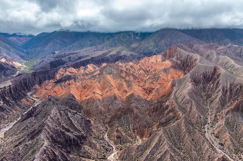 Breathtaking aerial view of the Hill of Seven Colors in Purmamarca, Argentina, showcasing vibrant layers of multicolored mountains under a cloudy sky, highlighting natural beauty