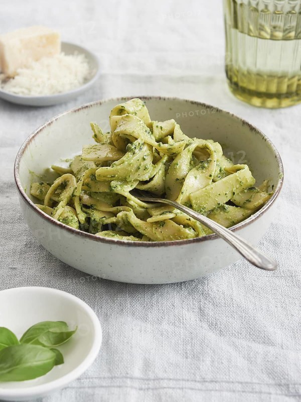 Close-up of green pasta bowl with fork on green Tagliatelle pesto beside basil leaves and parmesan cheese. Traditional Italian food