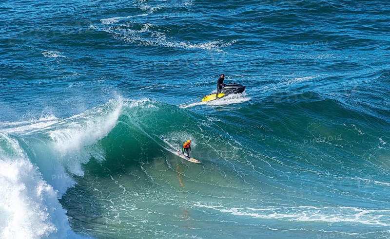 Surfers with their jet ski pilots in the Atlantic waves below Farol de Nazaré, Forte São Miguel, known as a surfer hot spot with monster waves between November and February of each year, Nazaré, Portugal