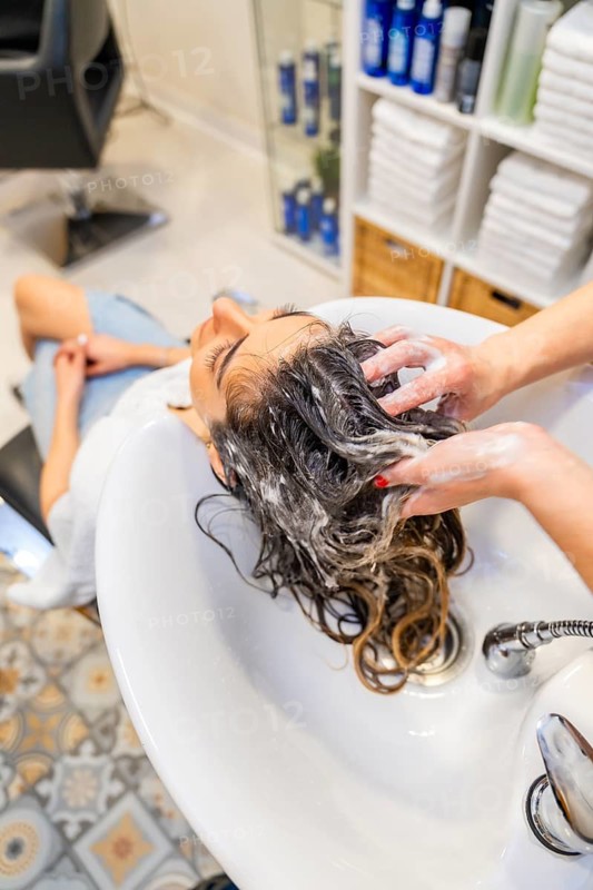 Top view of a hairdresser repairing the damaged hair of a woman with cosmetics washing her hair